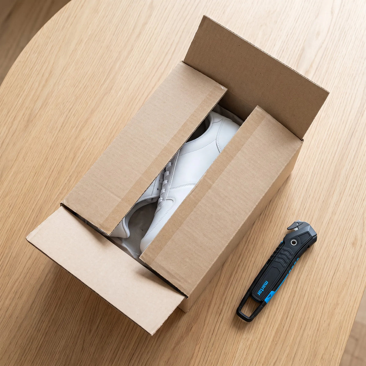 Sauber geöffneter Versandkarton mit unversehrten Sneakern, daneben der MARTOR SECUMAX 350 auf dem Holztisch – SICHERHEITSCUTTER.DE