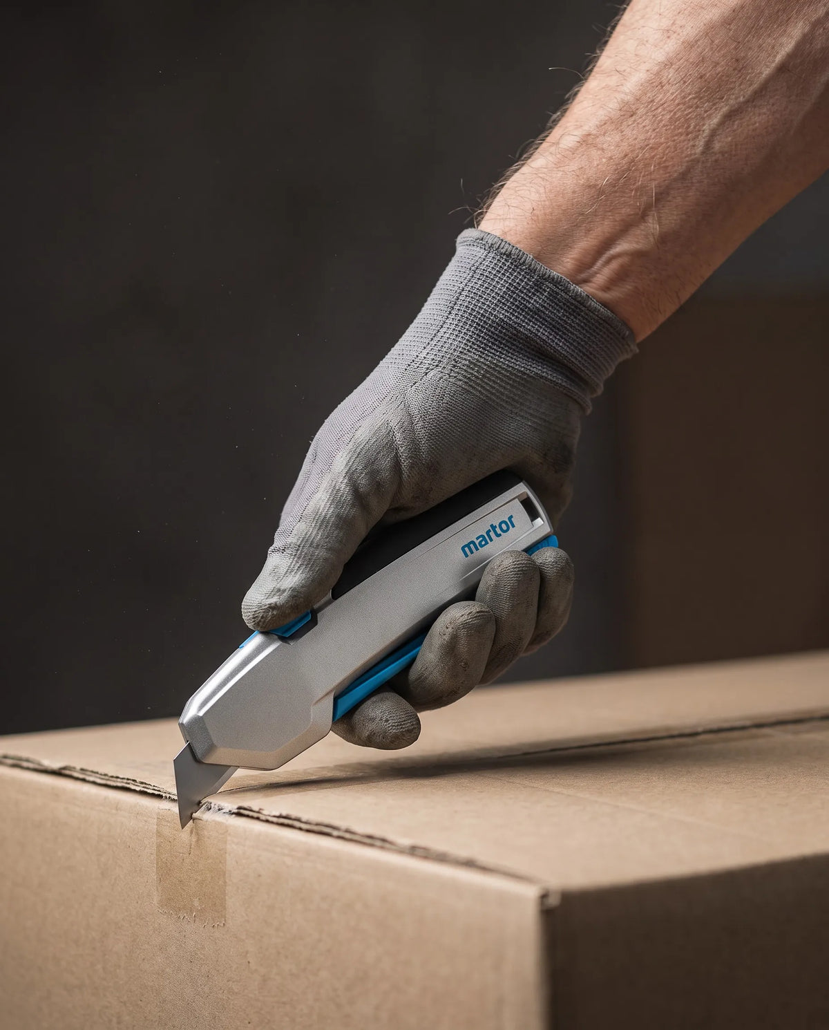 Hand im Arbeitshandschuh schneidet einen Karton mit dem MARTOR SECUPRO 625 mit Aluminiumgriff – SICHERHEITSCUTTER.DE